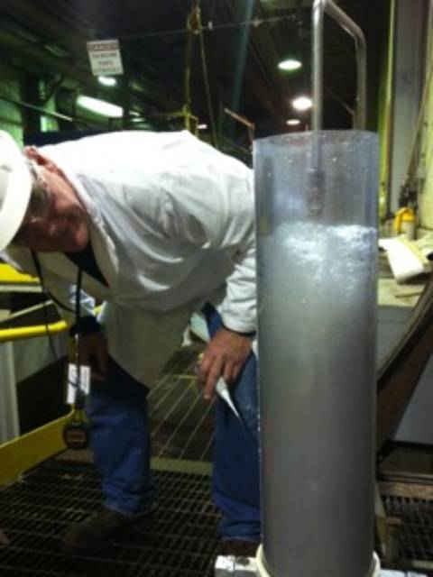 A man in white shirt and hat next to a metal object.